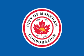 A blue background with a Red and White circle. The red and white circle says "The City of Markham Corporation" with 1850, 1872, 1971, 2012 around a red maple leaf with a gold beaver in the middle.