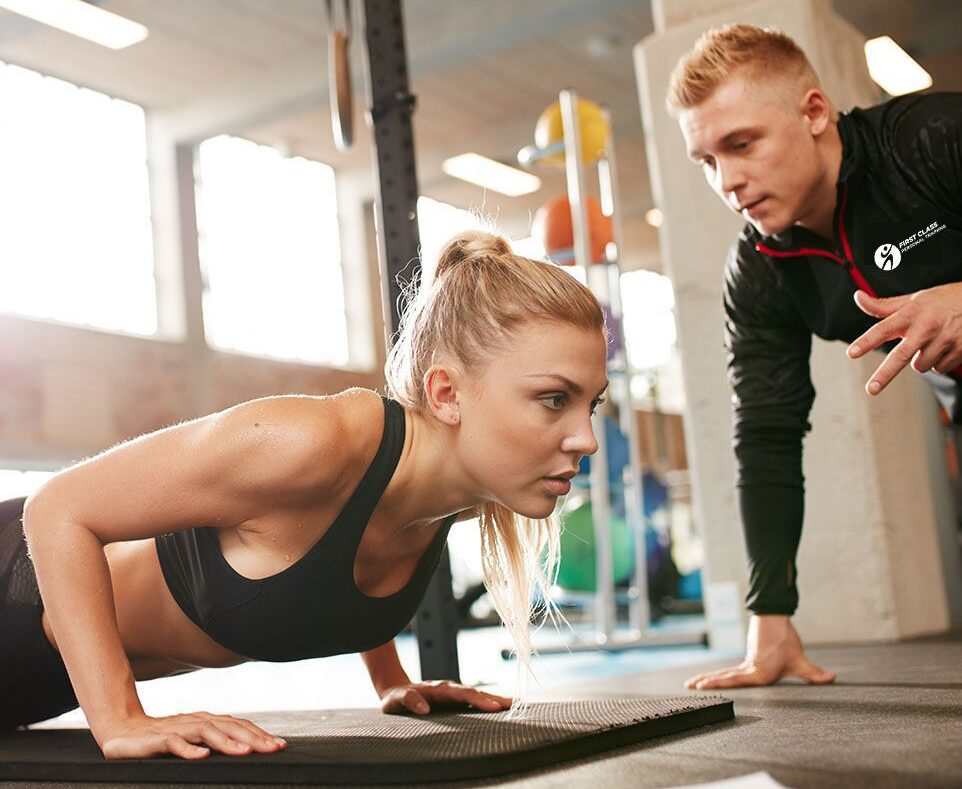 A male personal trainer coaches a female client doing pushups.