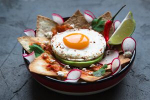 An image of a traditional Mexican breakfast dish: chilaquiles with egg, avocado and vegetables close-up on a plate.