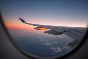 An image of the window seat view inside an airplane overlooking the left wing and the horizon at dawn